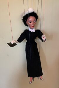 Marionette lady dressed in 1950s dress, with black handbag and white feathered pillbox hat